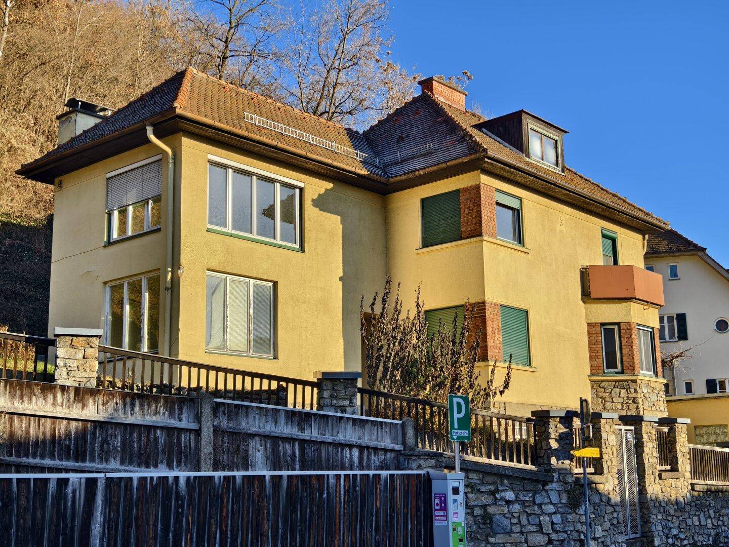 Gelbes Gebäude mit Ziegeldach und Steinfassade, umgeben von einer Steinmauer.