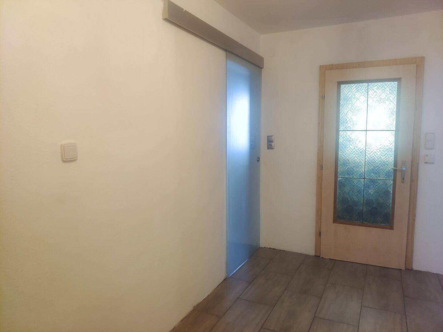 Heller Eingangsbereich mit Fliesenboden und Schiebetür aus Milchglas.