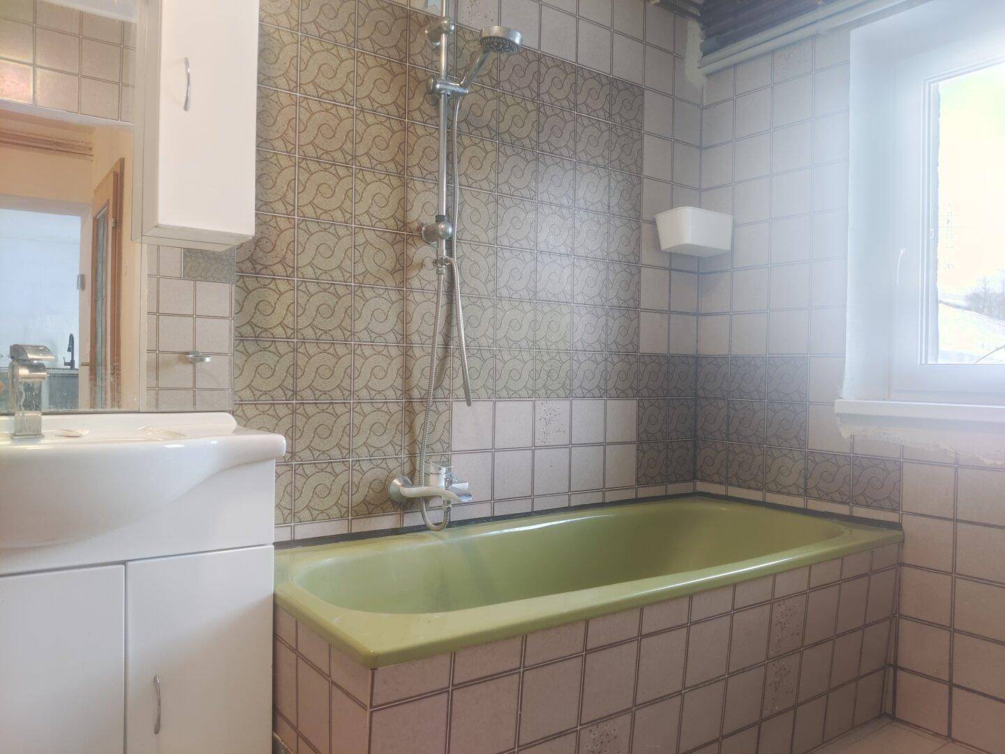 Badezimmer mit grüner Badewanne, Duschvorrichtung und gemusterten Fliesen.