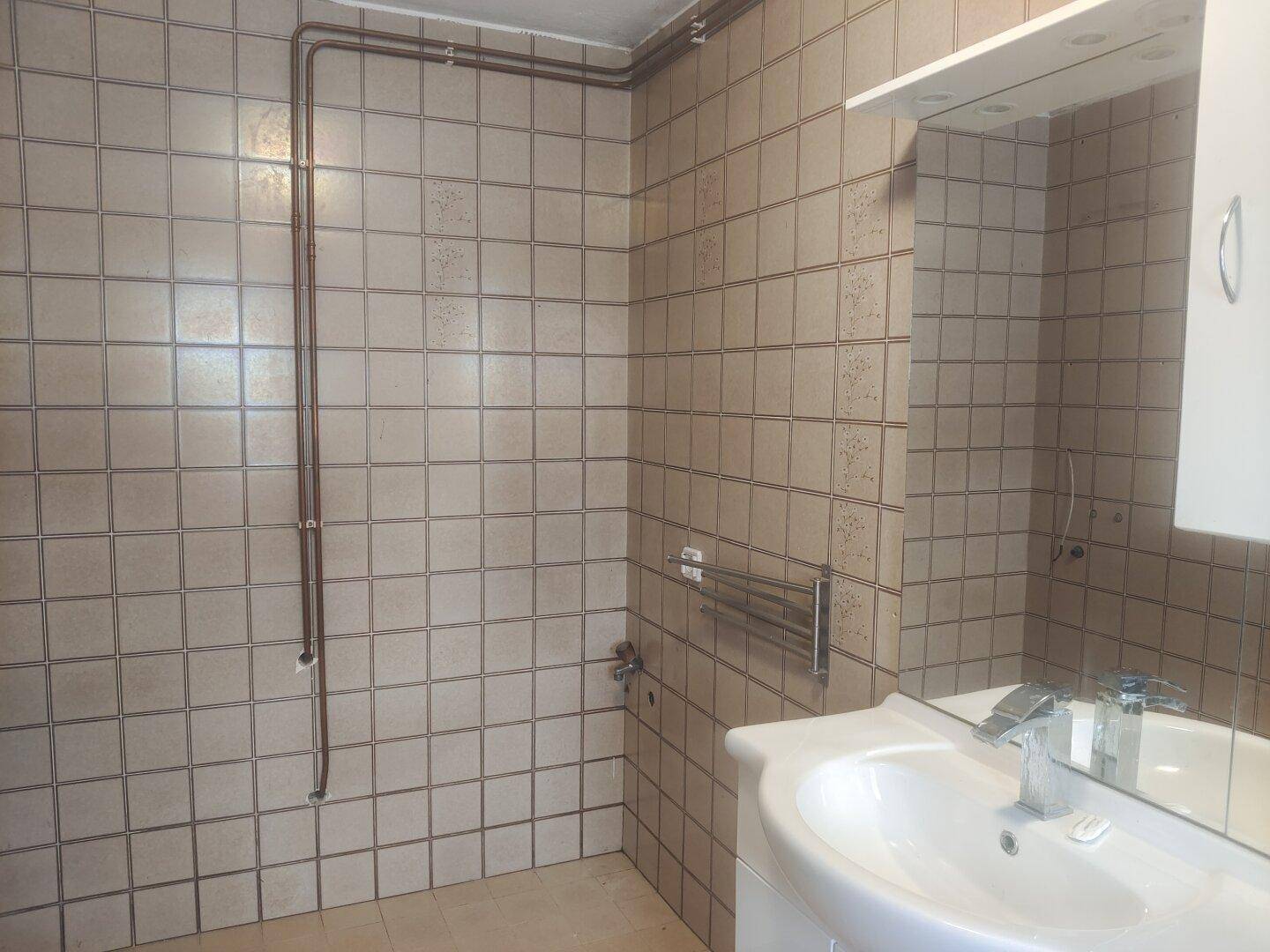 Badezimmer mit Waschbecken, Spiegel und beigefarbenen Wandfliesen.