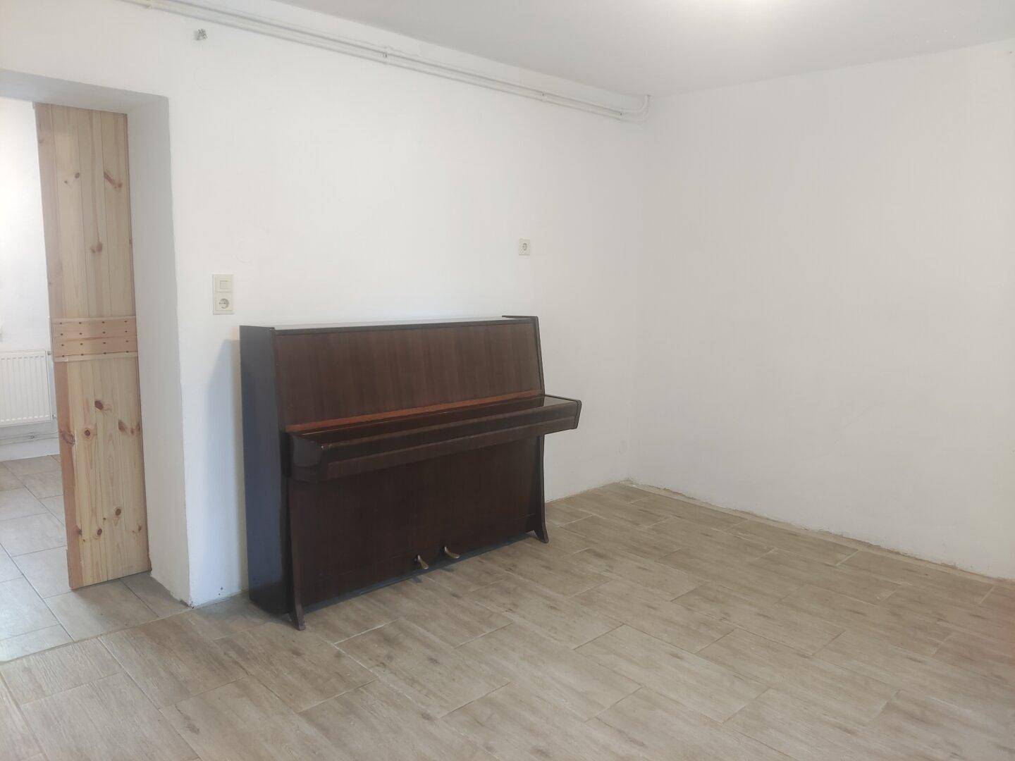 Geräumiger Raum mit Fliesenboden und einem Klavier, ideal als Wohn- oder Musikzimmer.