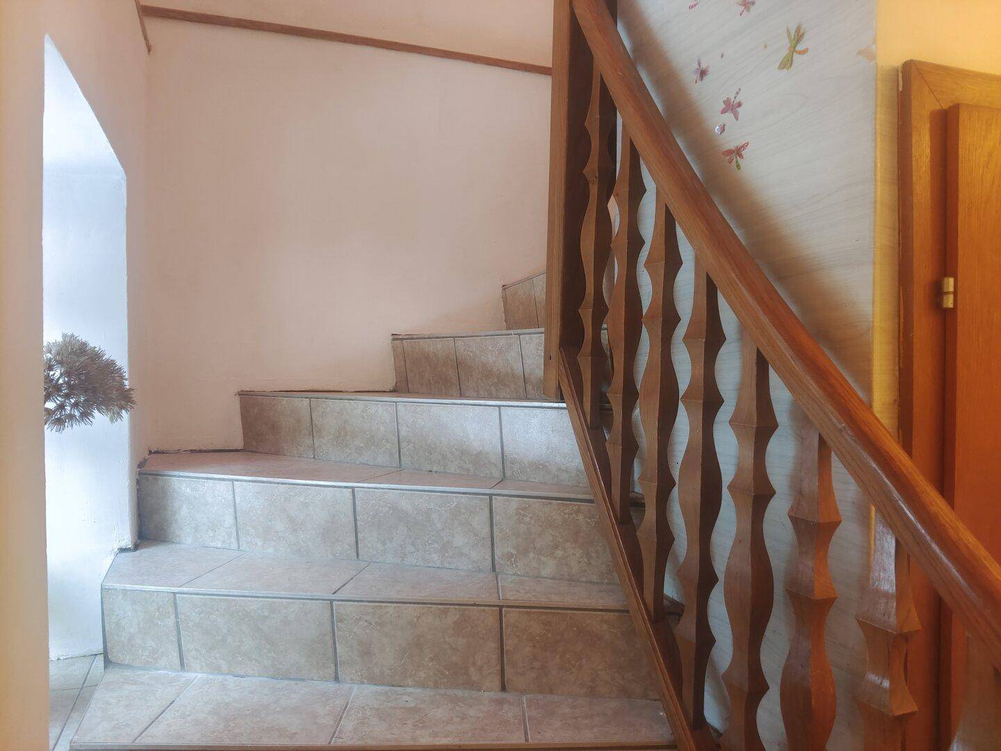 Treppenaufgang mit Holzgeländer und gefliesten Stufen, führt in die obere Etage.