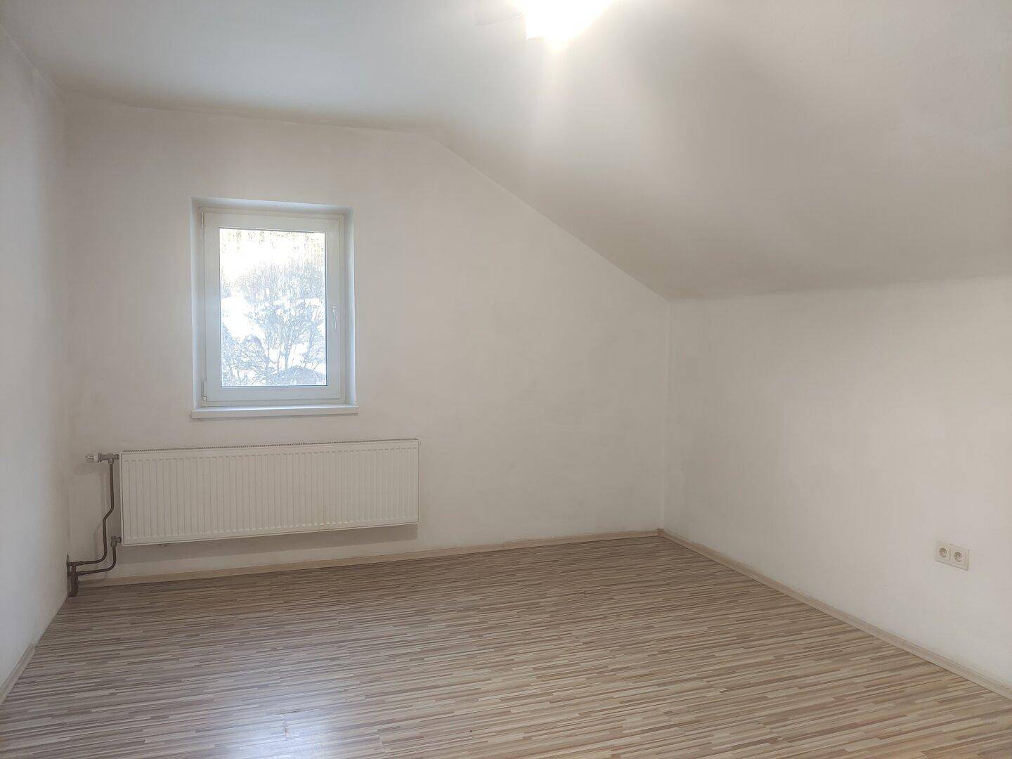 Helles Zimmer im Dachgeschoss mit Schrägdecke, Fenster und Laminatboden.