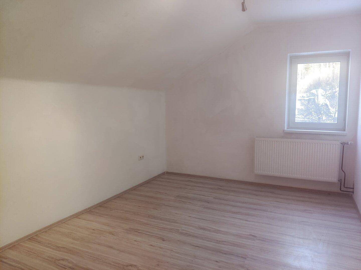 Geräumiges Dachzimmer mit Schrägdecke, Laminatboden und Fenster mit Ausblick.