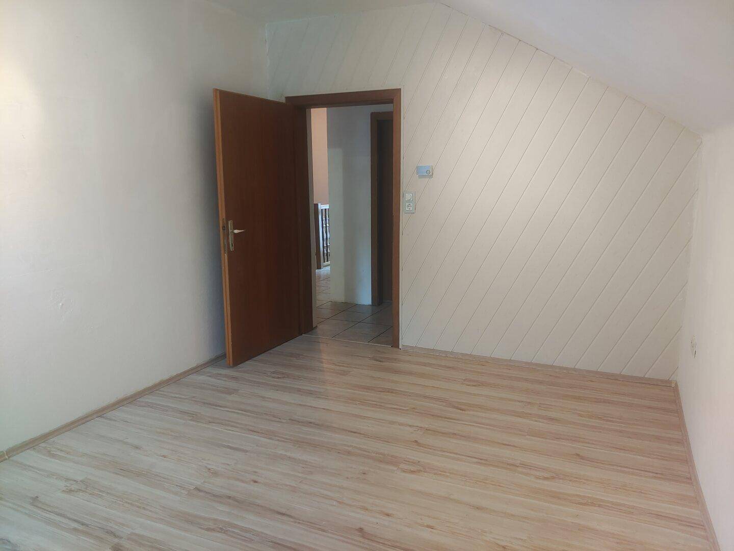 Dachzimmer mit Schrägdecke, Laminatboden und dekorativer Holzverkleidung an der Wand.