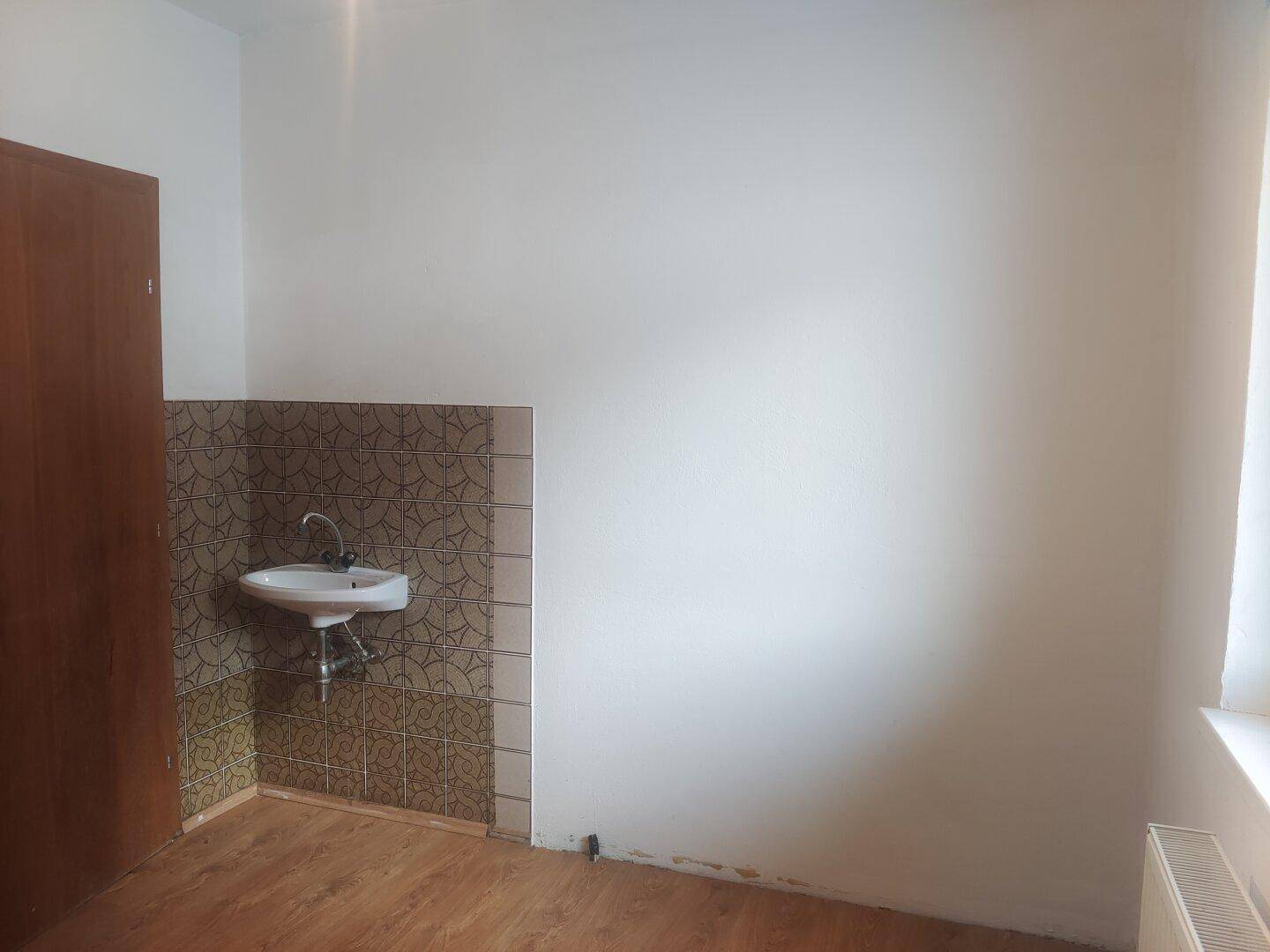 Raum mit kleinem Waschbecken und gefliestem Bereich, vielseitig nutzbar.