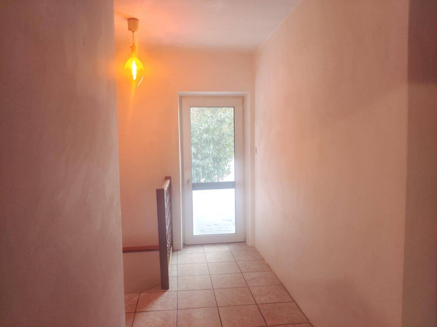 Heller Flur mit Fliesenboden und einer Tür, die ins Freie führt.