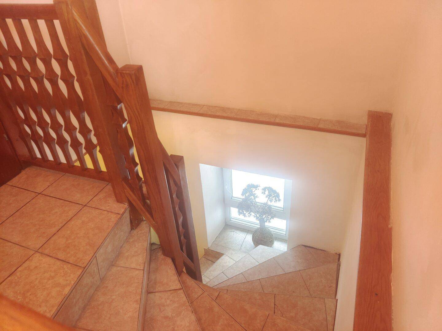 Blick von oben auf den gefliesten Treppenaufgang mit Holzgeländer und Fenster.