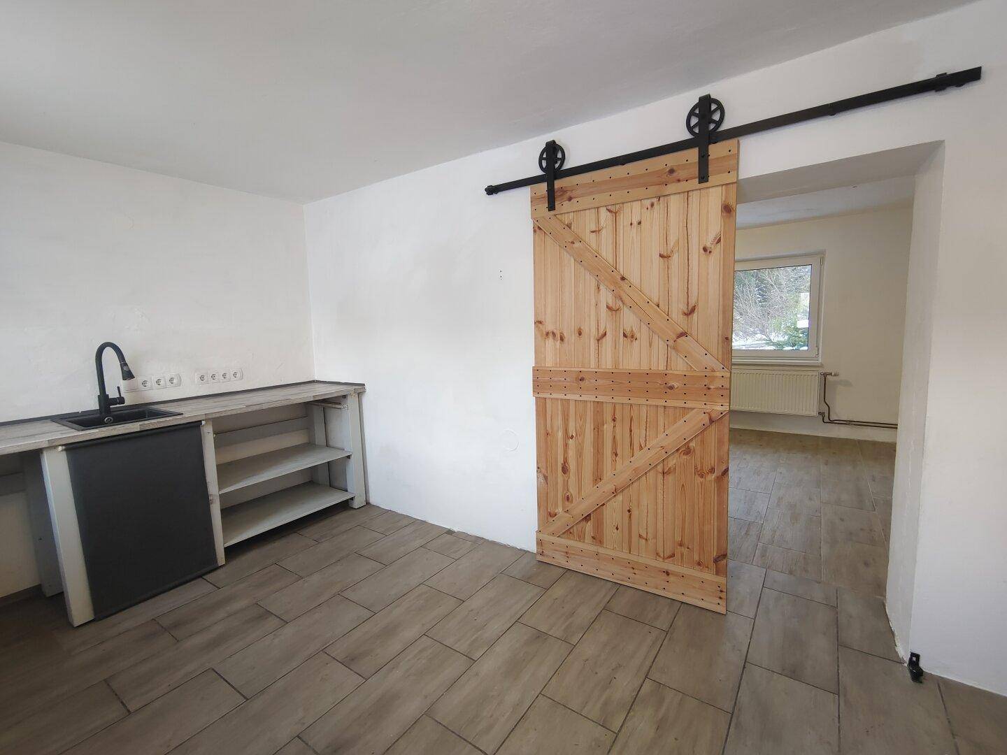Nutzraum mit Waschbecken, einfacher Arbeitsplatte und rustikaler Schiebetür.