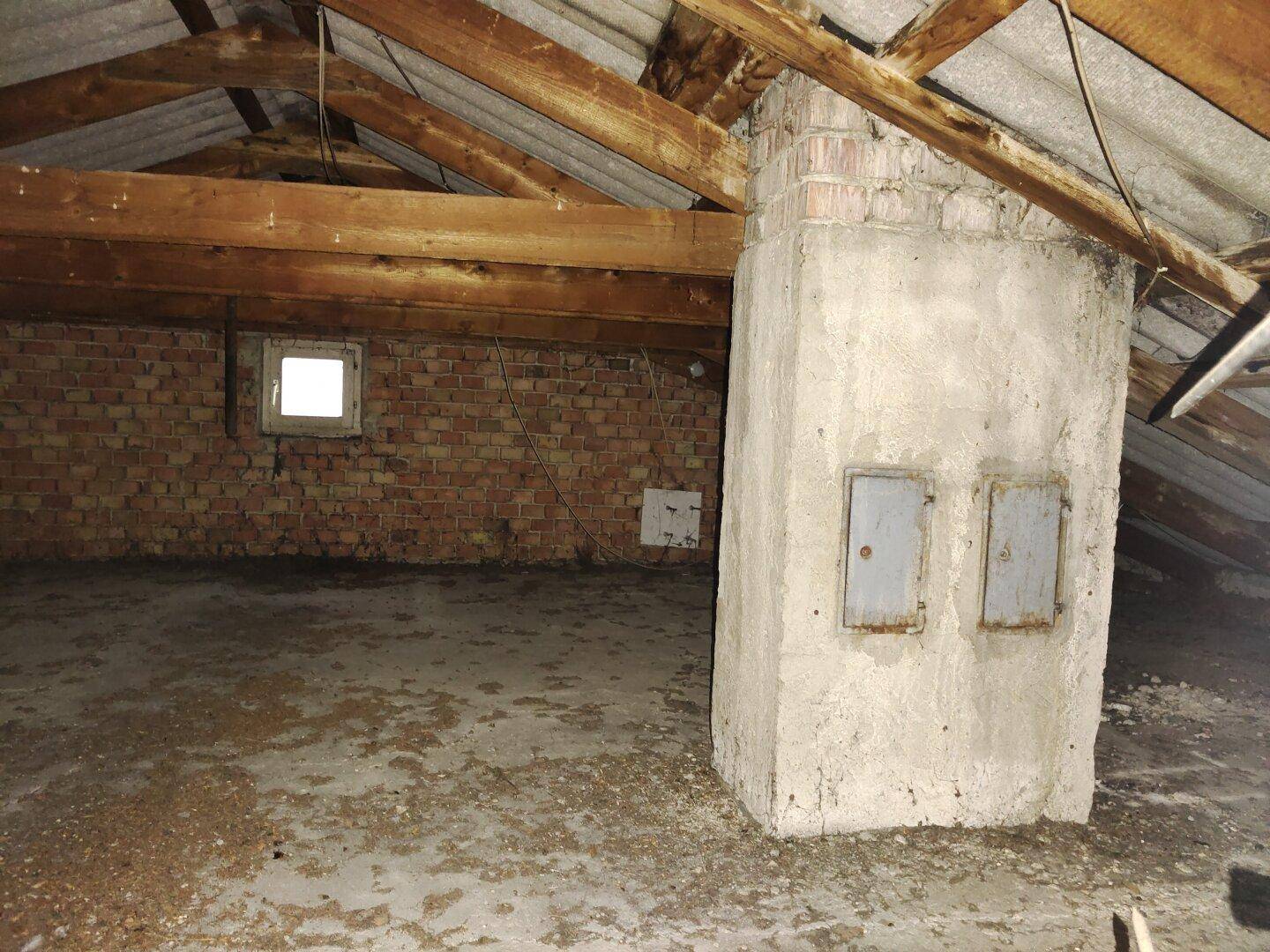 Dachboden mit sichtbaren Holzbalken, Ziegelwänden und einem kleinen Fenster.