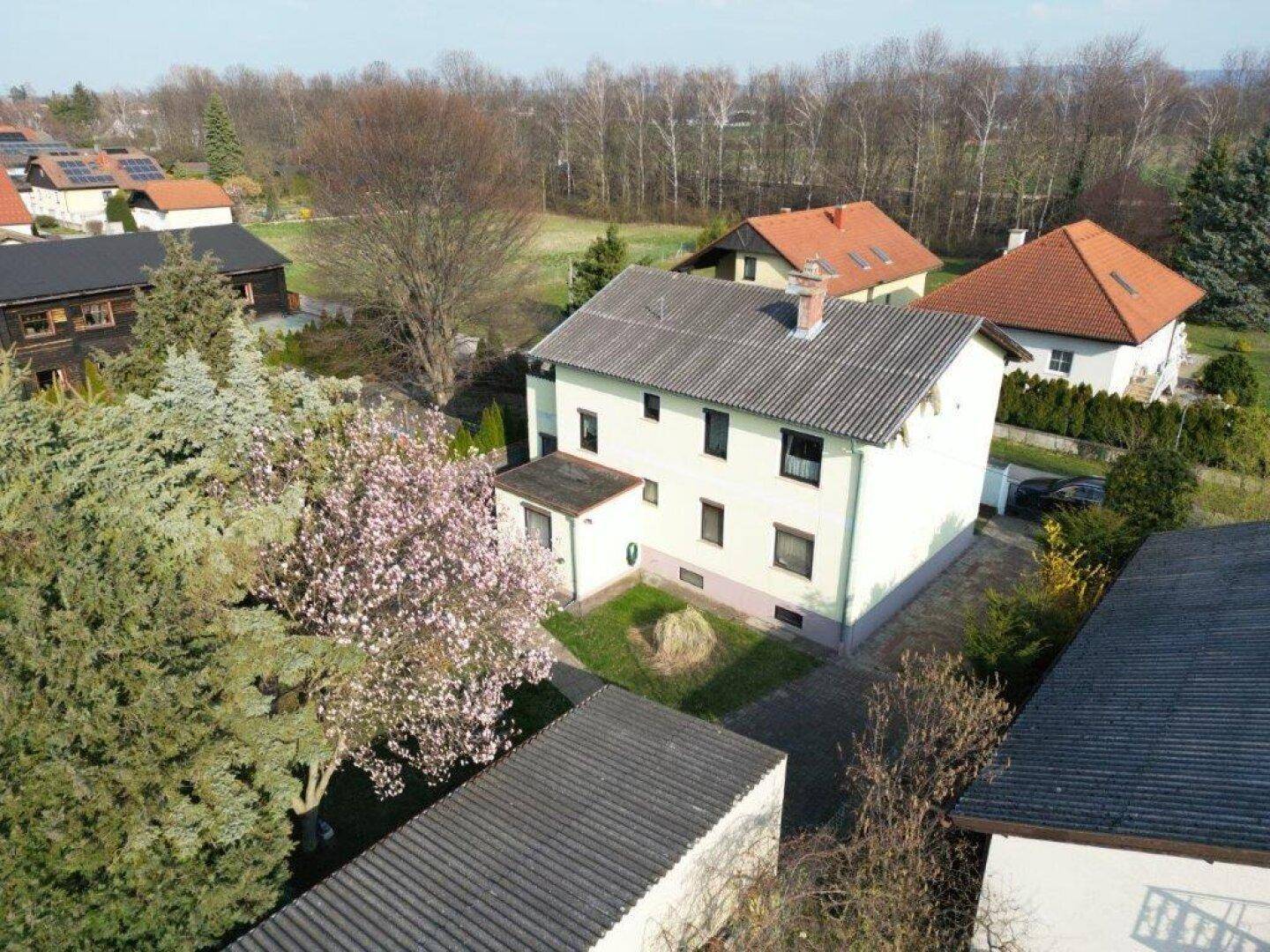 Luftaufnahme des Wohnhauses mit umliegenden Gärten und Dächern in einer ruhigen Nachbarschaft.