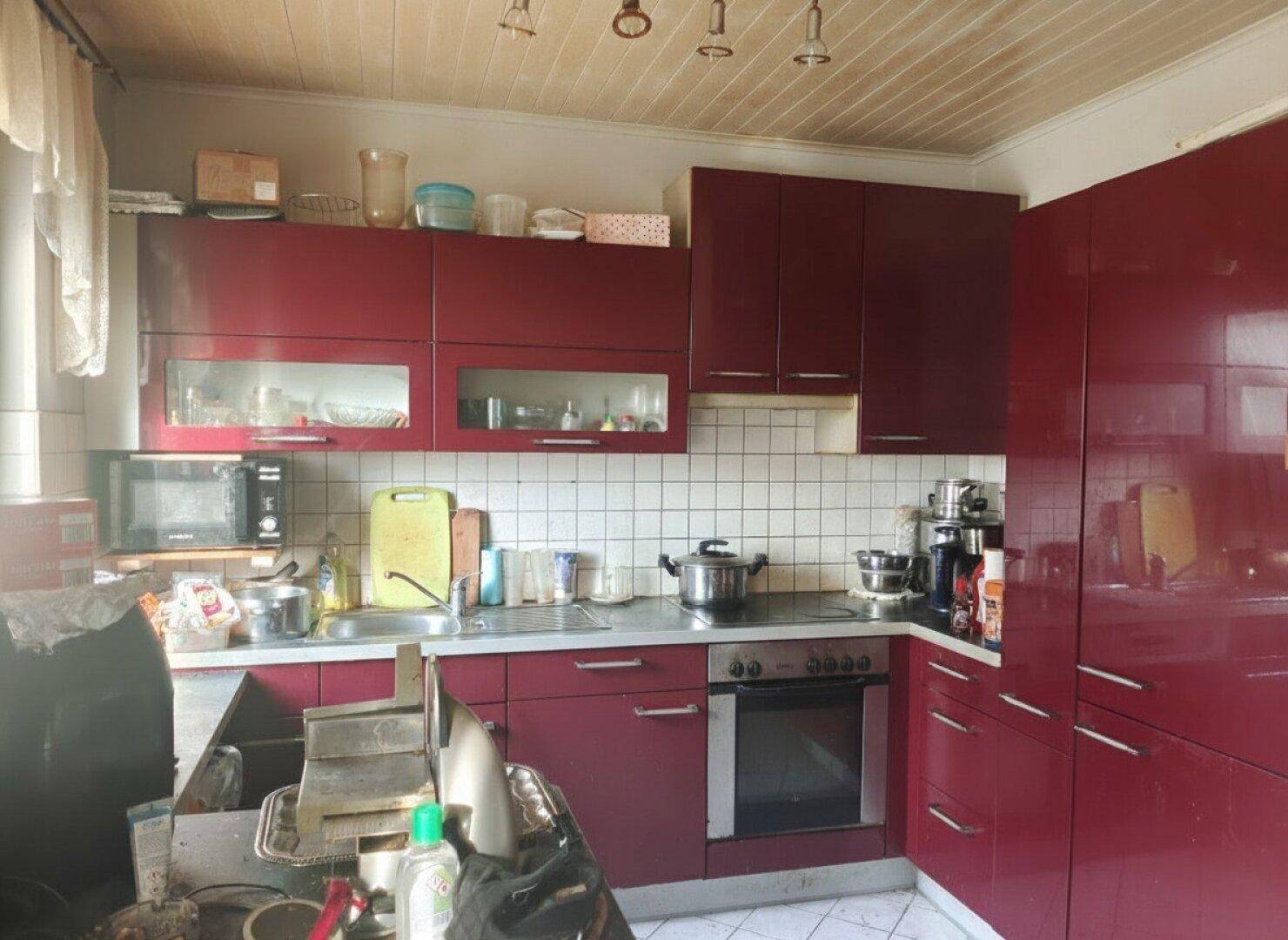 Küche mit roten Hochglanzschränken, weißen Fliesen und einem Herd mit Backofen.