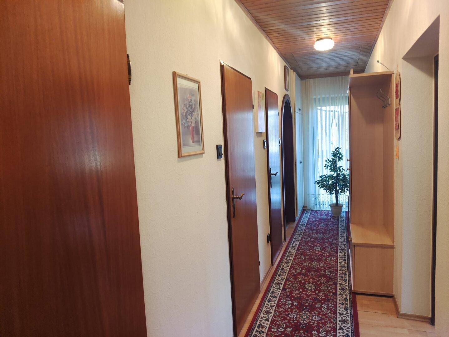 Langer Flur mit Holzdecke, Teppichläufer und mehreren Türen zu den angrenzenden Zimmern.