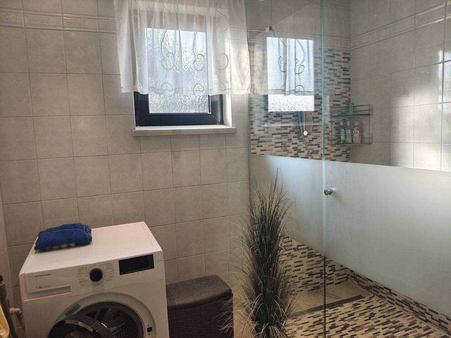 Modernes Badezimmer mit begehbarer Dusche, Waschmaschine und einem Fenster für Tageslicht.