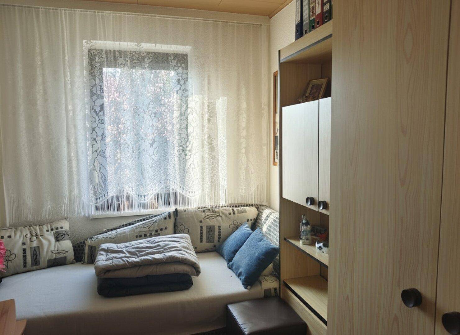 Kleines Schlafzimmer oder Gästezimmer mit Bett, Regalen und einem Fenster für natürliches Licht.