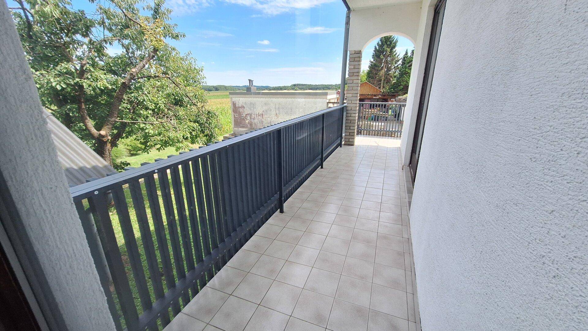 Langer Balkon mit Fliesenboden und dunklem Geländer, bietet weite Aussicht.