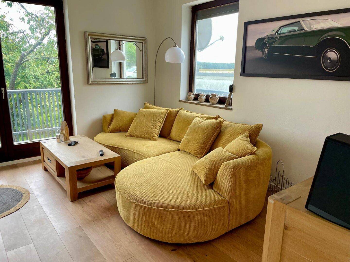 Gemütliches Wohnzimmer mit gelbem Sofa, Holzboden und Blick ins Grüne.