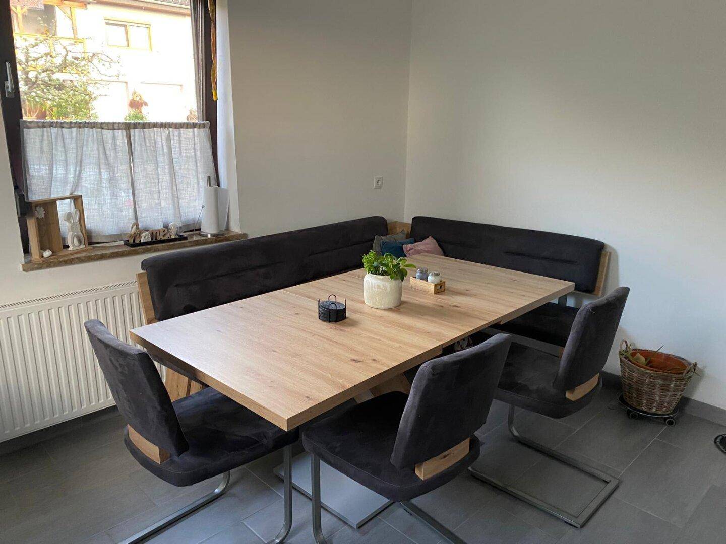 Gemütlicher Essbereich mit Holztisch, Eckbank und Stühlen neben einem Fenster.