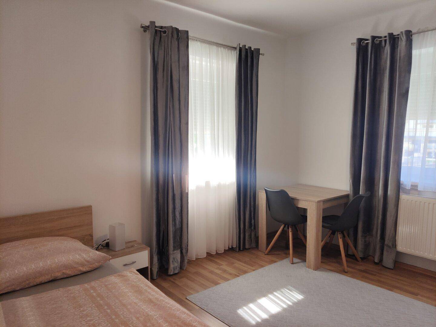 Helles Schlafzimmer mit Holzboden, zwei Einzelbetten und einem kleinen Schreibtisch.