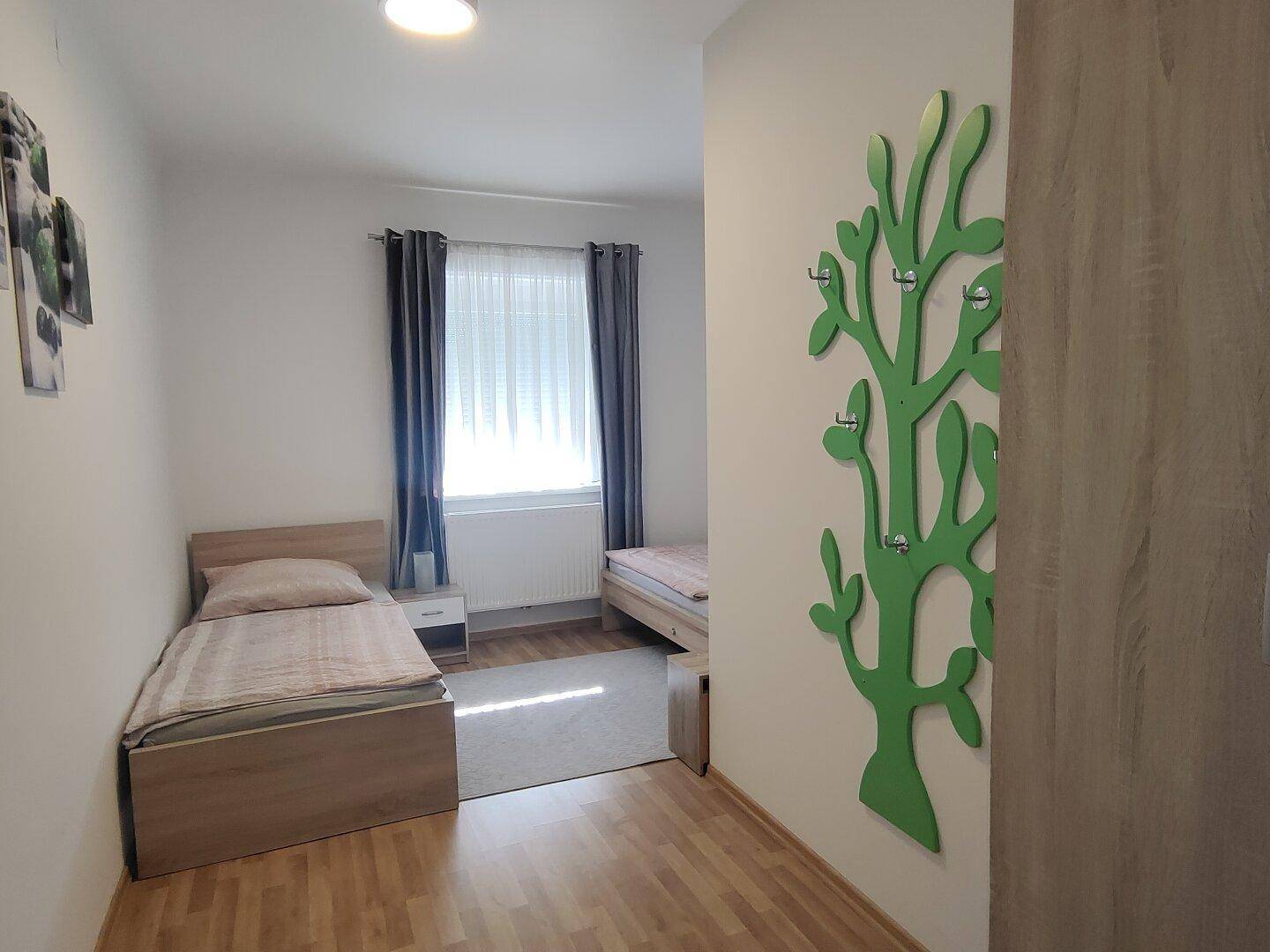 Schlafzimmer mit zwei Einzelbetten, Holzboden und einem dekorativen Wandelement.