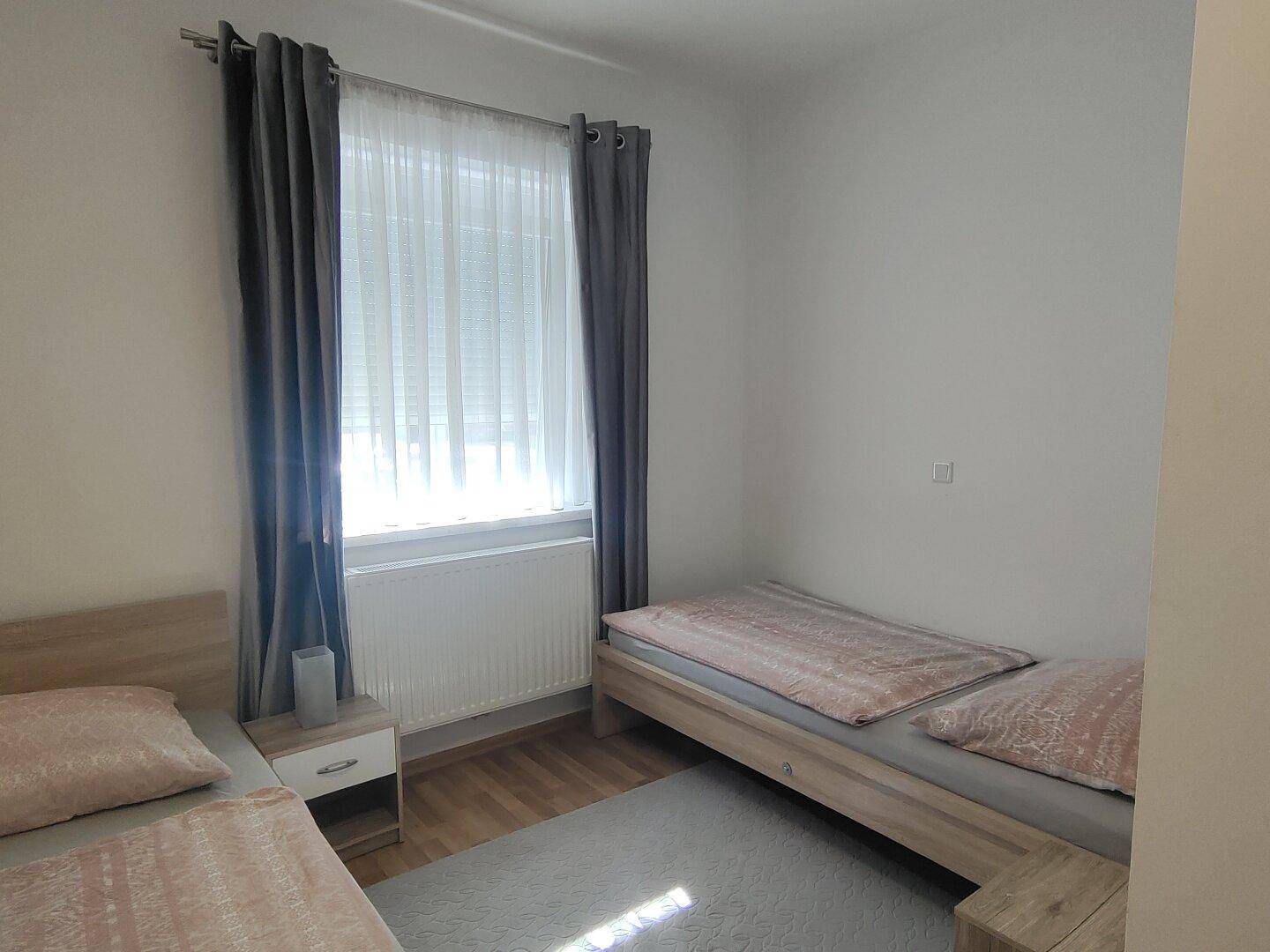 Helles Schlafzimmer mit zwei Einzelbetten, Holzboden und großem Fenster.