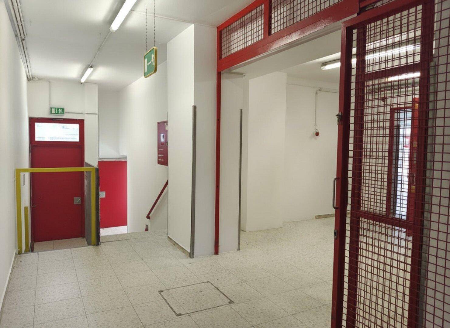 Eingangsbereich mit Fliesenboden, rotem Gitter und Treppenaufgang.