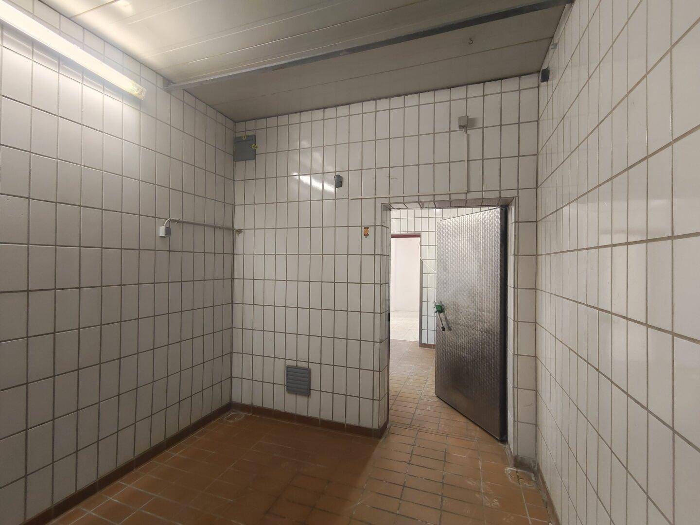 Gefliester Raum mit weißen Wandfliesen und braunem Boden, möglicherweise ein Lagerraum.