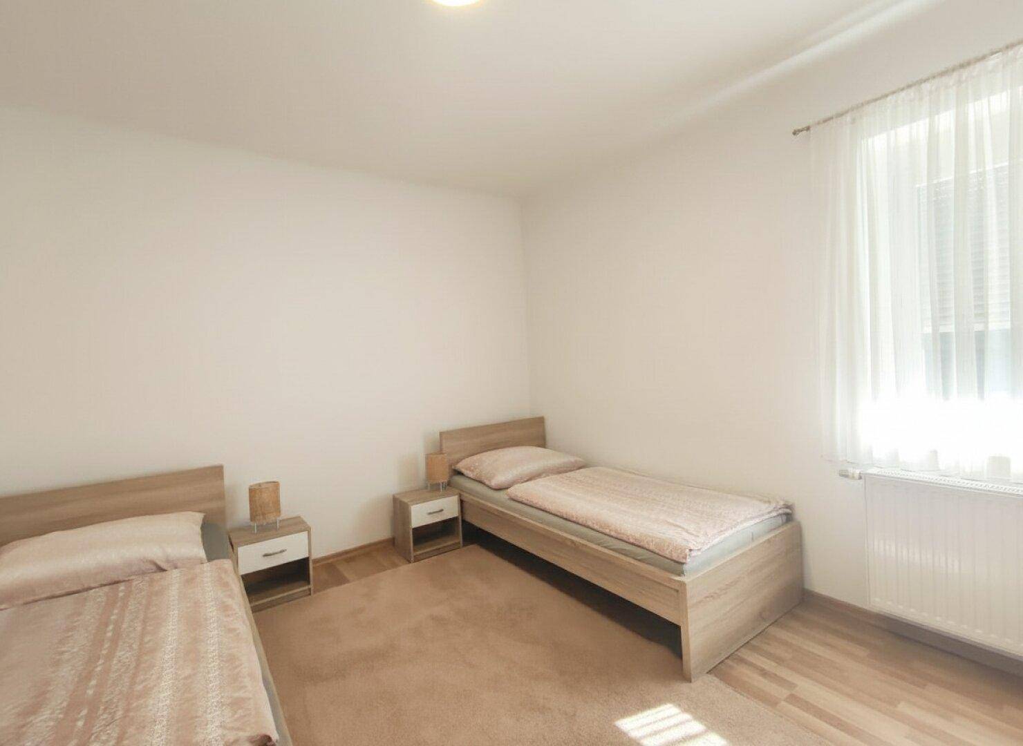 Schlafzimmer mit zwei Einzelbetten, Holzboden und einem Teppich in warmen Farben.