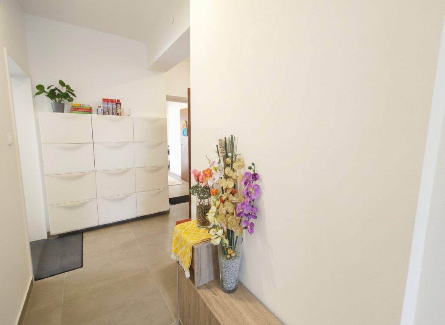 Heller Flur mit Fliesenboden, weißem Schuhschrank und dekorativen Blumen.
