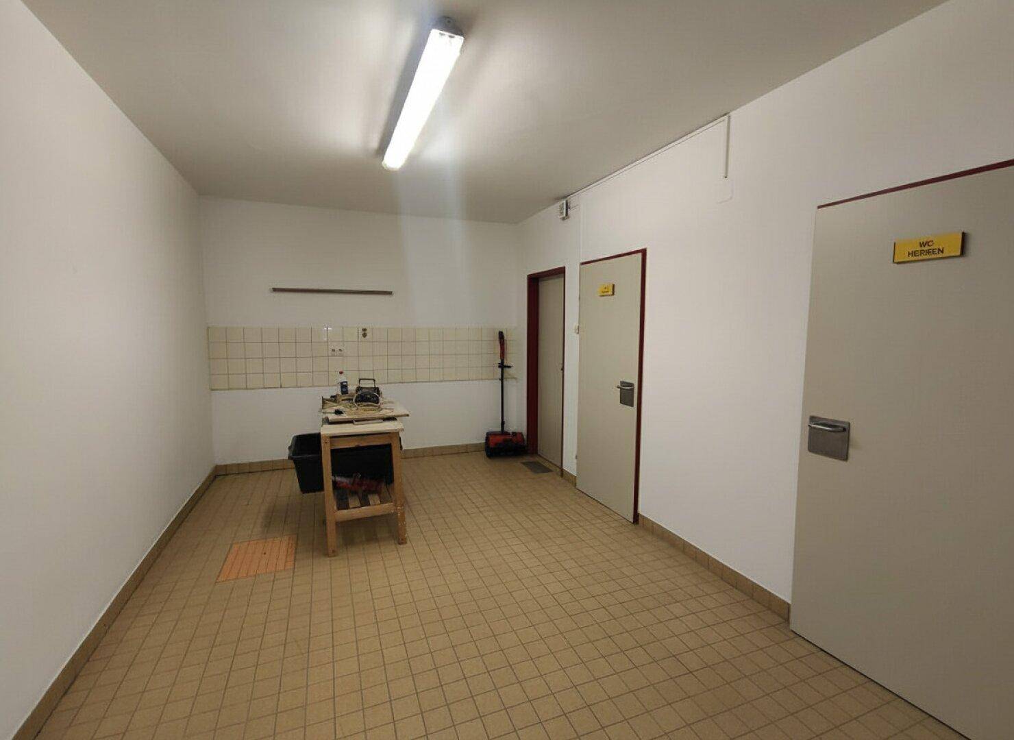Abstellraum mit Fliesenboden und Türen zu den Toilettenbereichen.