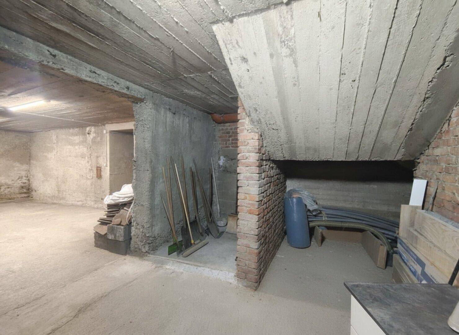 Kellerraum mit unverputzten Wänden, Betonboden und Lagerflächen.