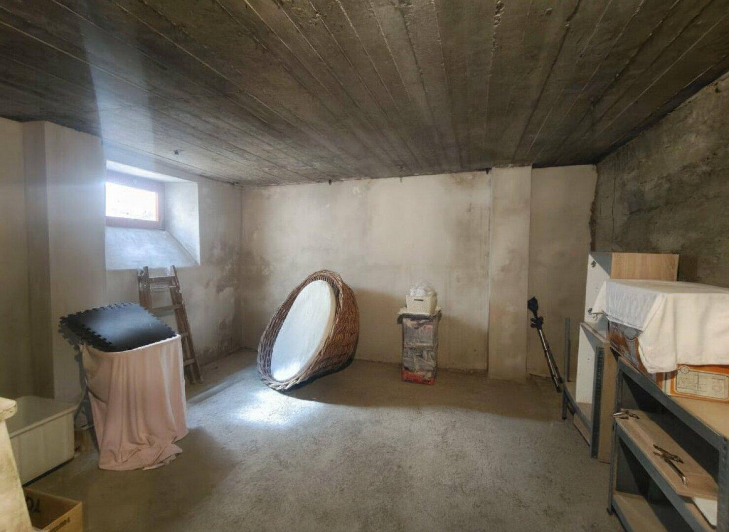 Heller Kellerraum mit kleinem Fenster, Betonboden und verschiedenen Gegenständen.