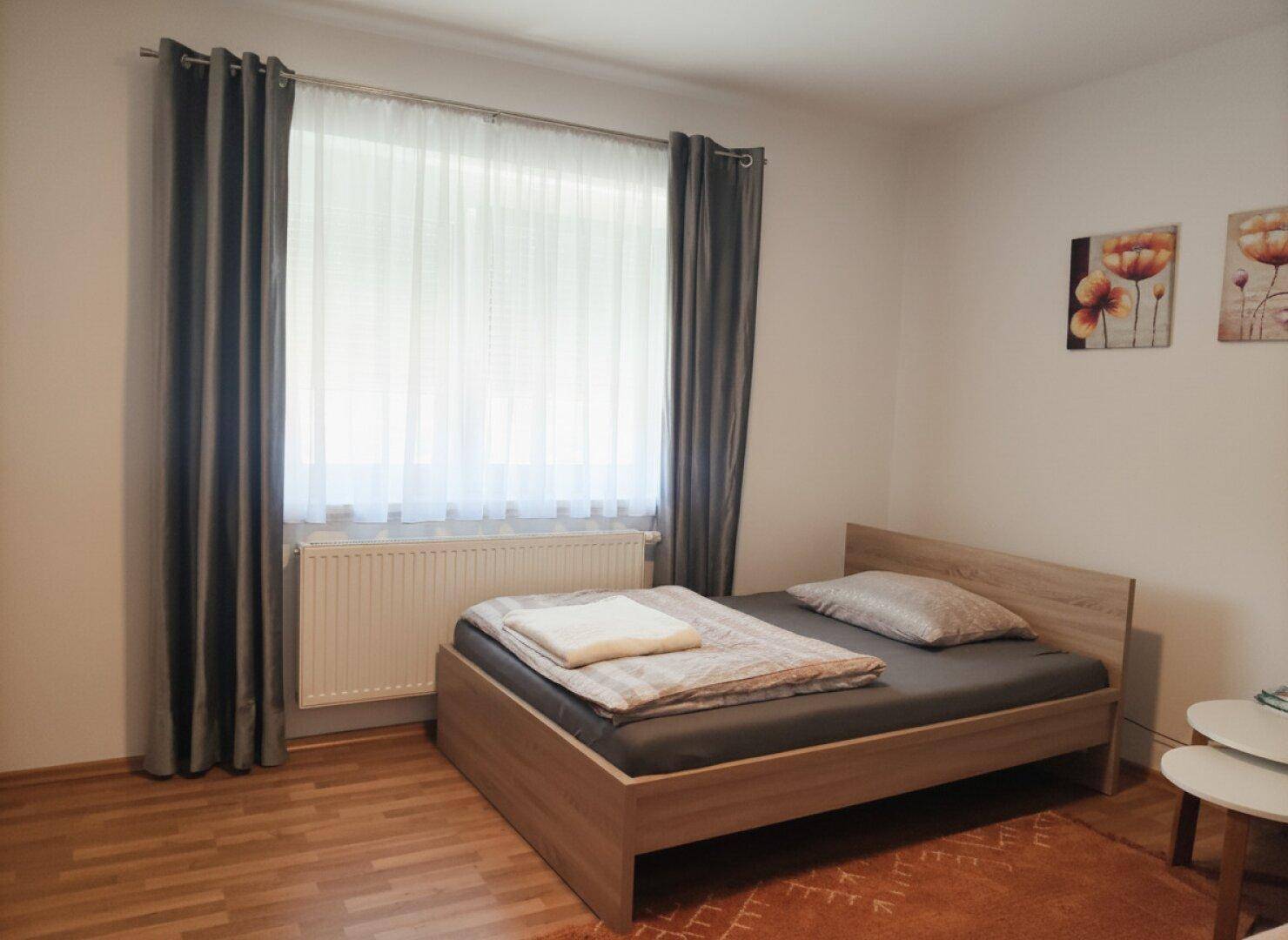 Schlafzimmer mit Holzboden, Einzelbett und farbigen Bildern an der Wand.