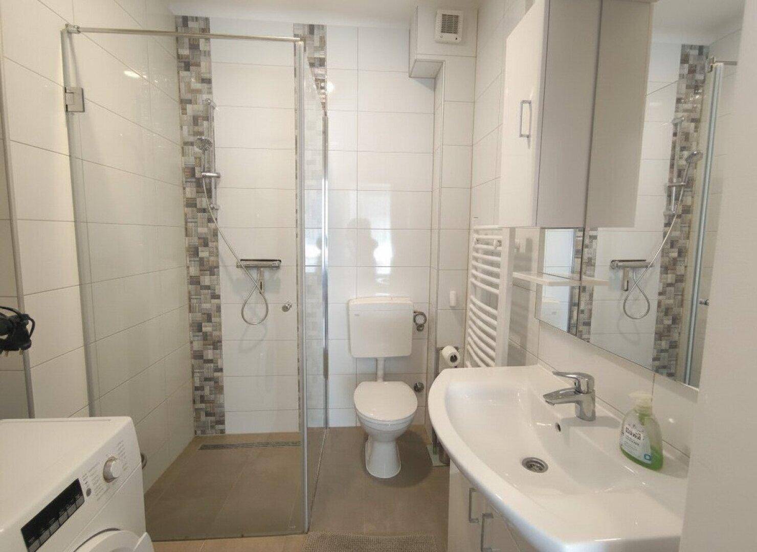 Modernes Badezimmer mit Duschkabine, WC, Waschbecken und Handtuchheizkörper.