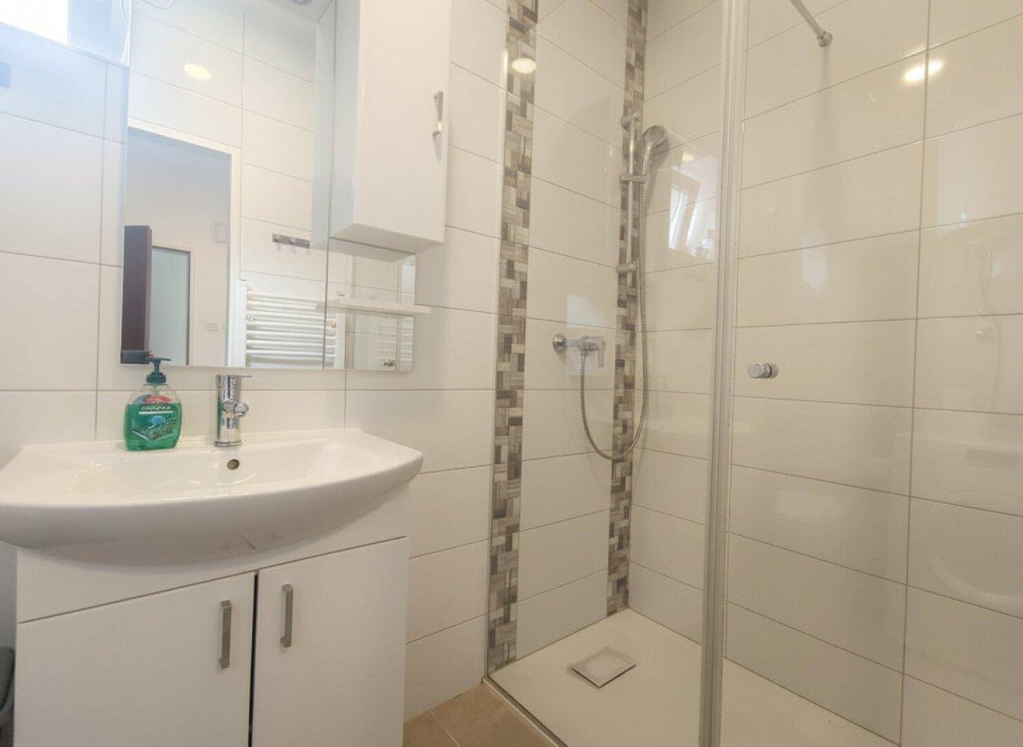 Helles Badezimmer mit Duschkabine, Waschbecken und Spiegelschrank.