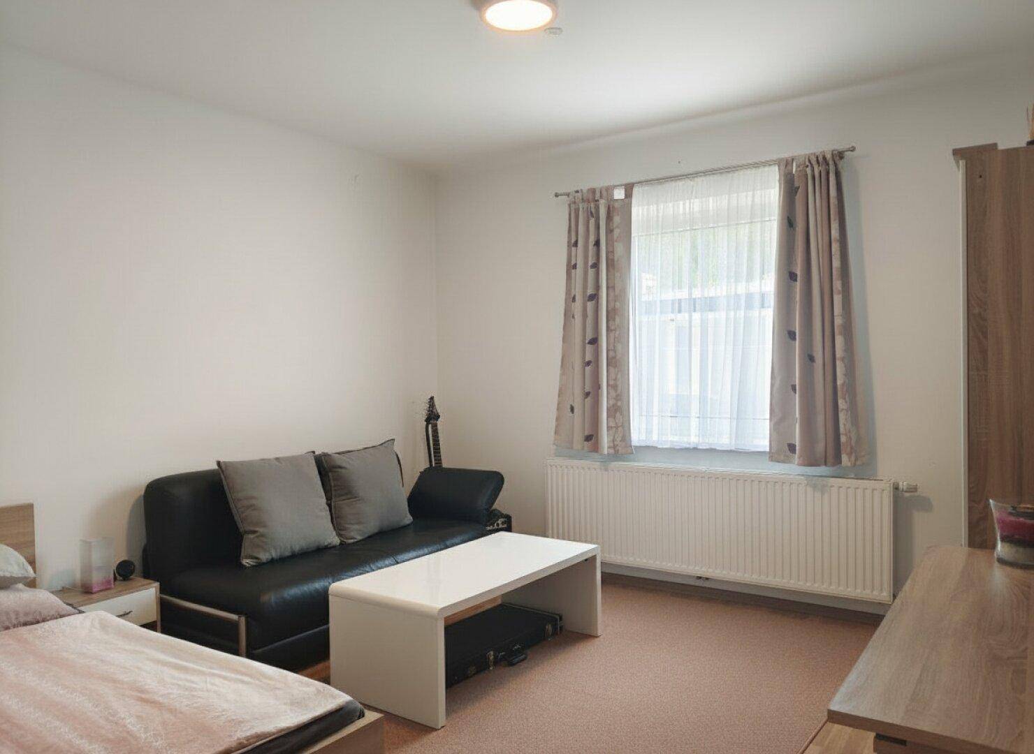 Schlafzimmer mit Sofa, Couchtisch und Teppichboden in neutralen Farben.