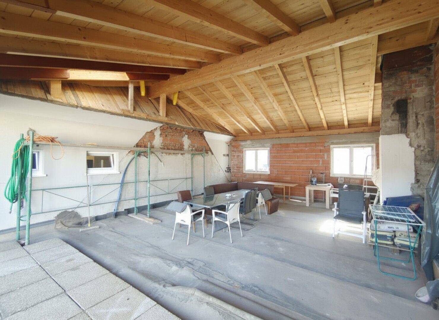 Ausbaufähiger Dachboden mit sichtbaren Holzbalken und Fenstern, bereit für den Ausbau.