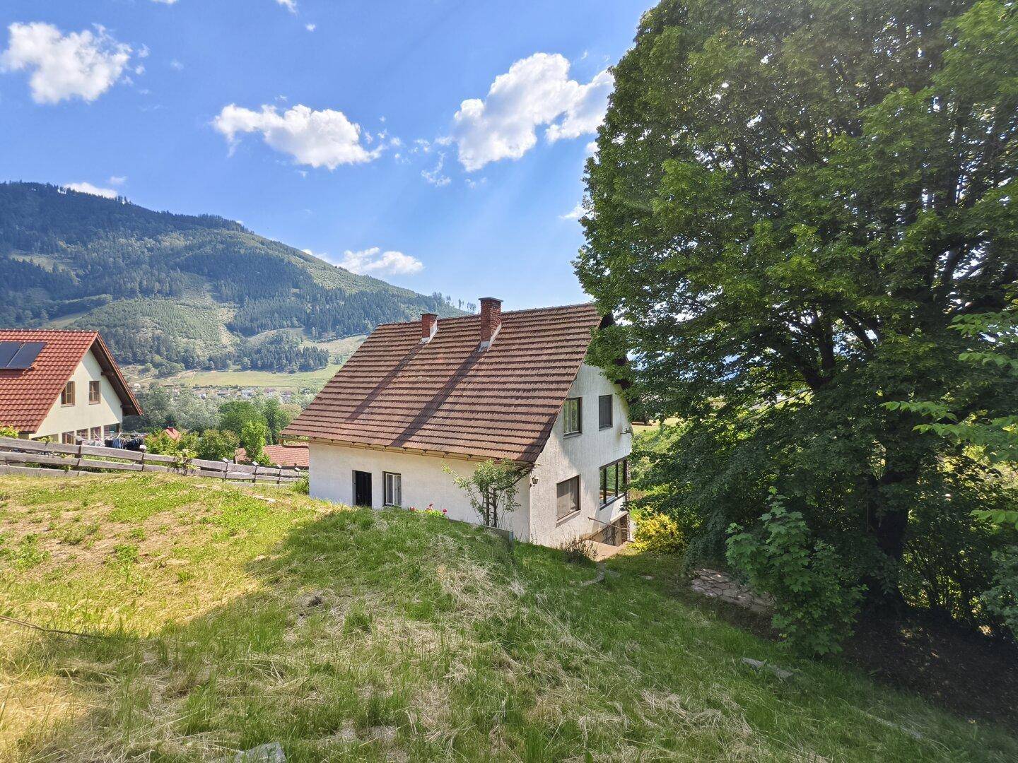 Haus auf einem Hügel mit weitem Blick über die grüne Landschaft und Berge.