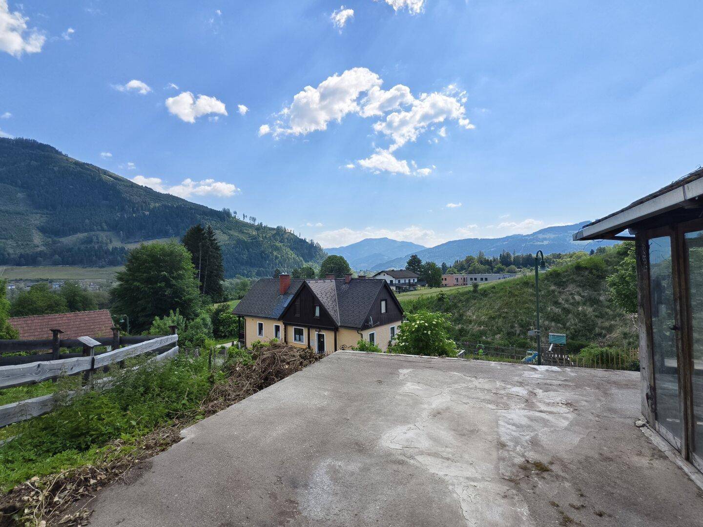Betonierte Fläche mit weitem Blick auf die grüne Berglandschaft und andere Häuser.
