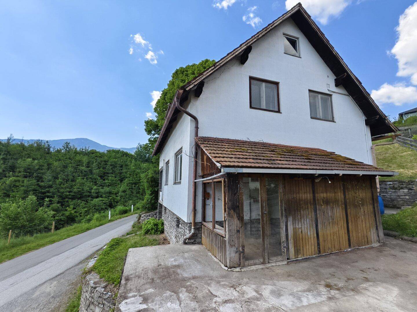 Seitenansicht des Hauses mit Holzanbau und Blick auf die bewaldete Umgebung.
