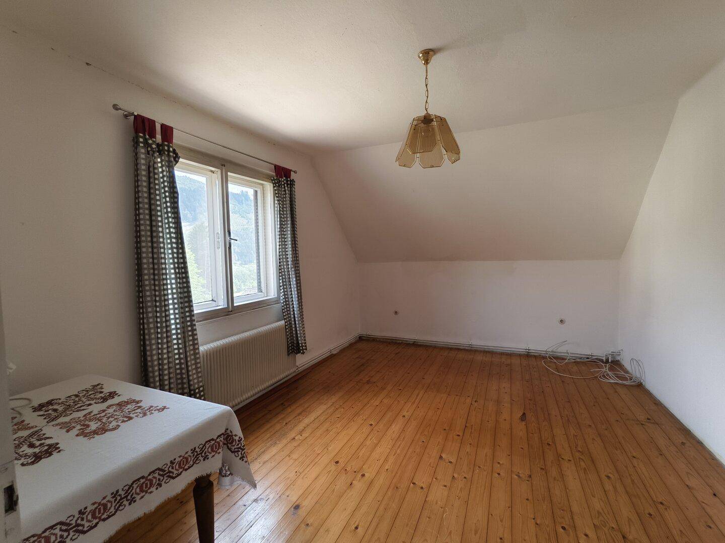 Helles Zimmer im Dachgeschoss mit Holzfußboden, Fenster und schräger Decke.