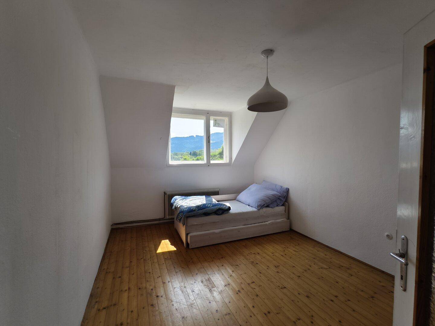 Schlafzimmer im Dachgeschoss mit Einzelbett, Holzfußboden und Fenster mit schöner Aussicht.