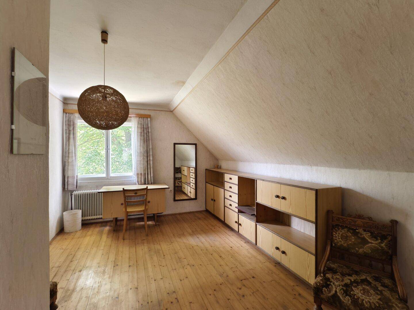 Geräumiges Zimmer im Dachgeschoss mit Holzfußboden, Schreibtisch und Stauraum.