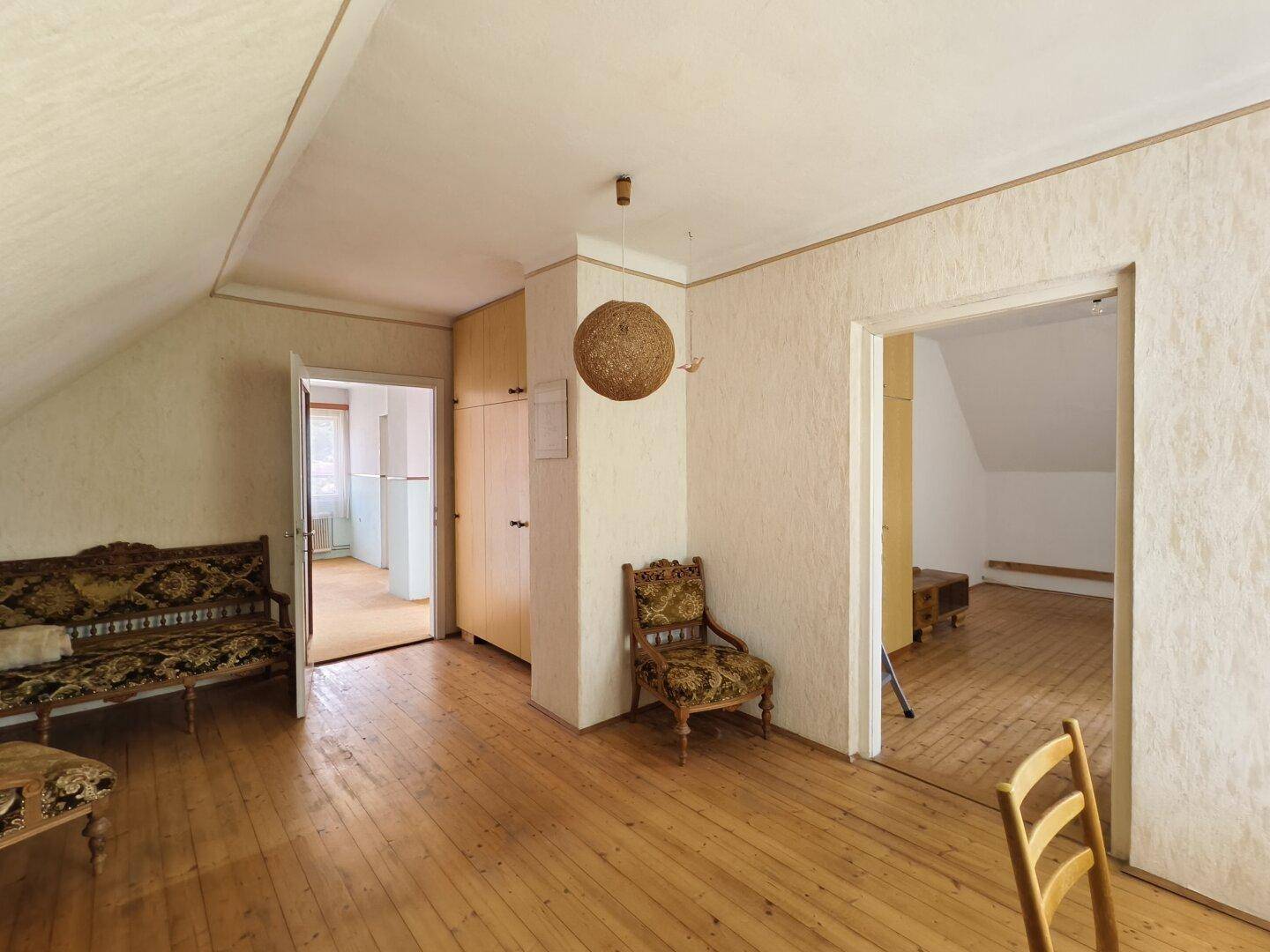 Wohnzimmer im Dachgeschoss mit Holzfußboden, antiken Möbeln und schräger Decke.