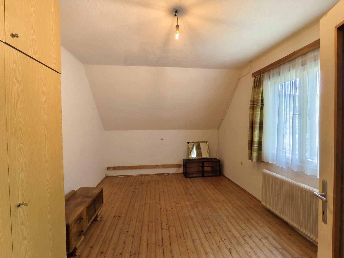 Helles Schlafzimmer im Dachgeschoss mit Holzfußboden, Fenster und Kleiderschrank.
