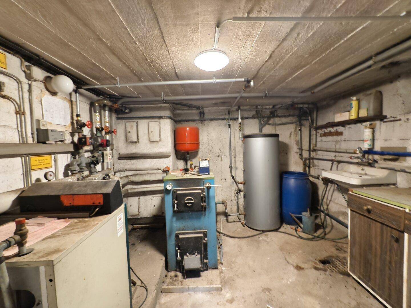 Heizungsraum im Keller mit alter Heizungsanlage, Rohren und Warmwasserspeicher.