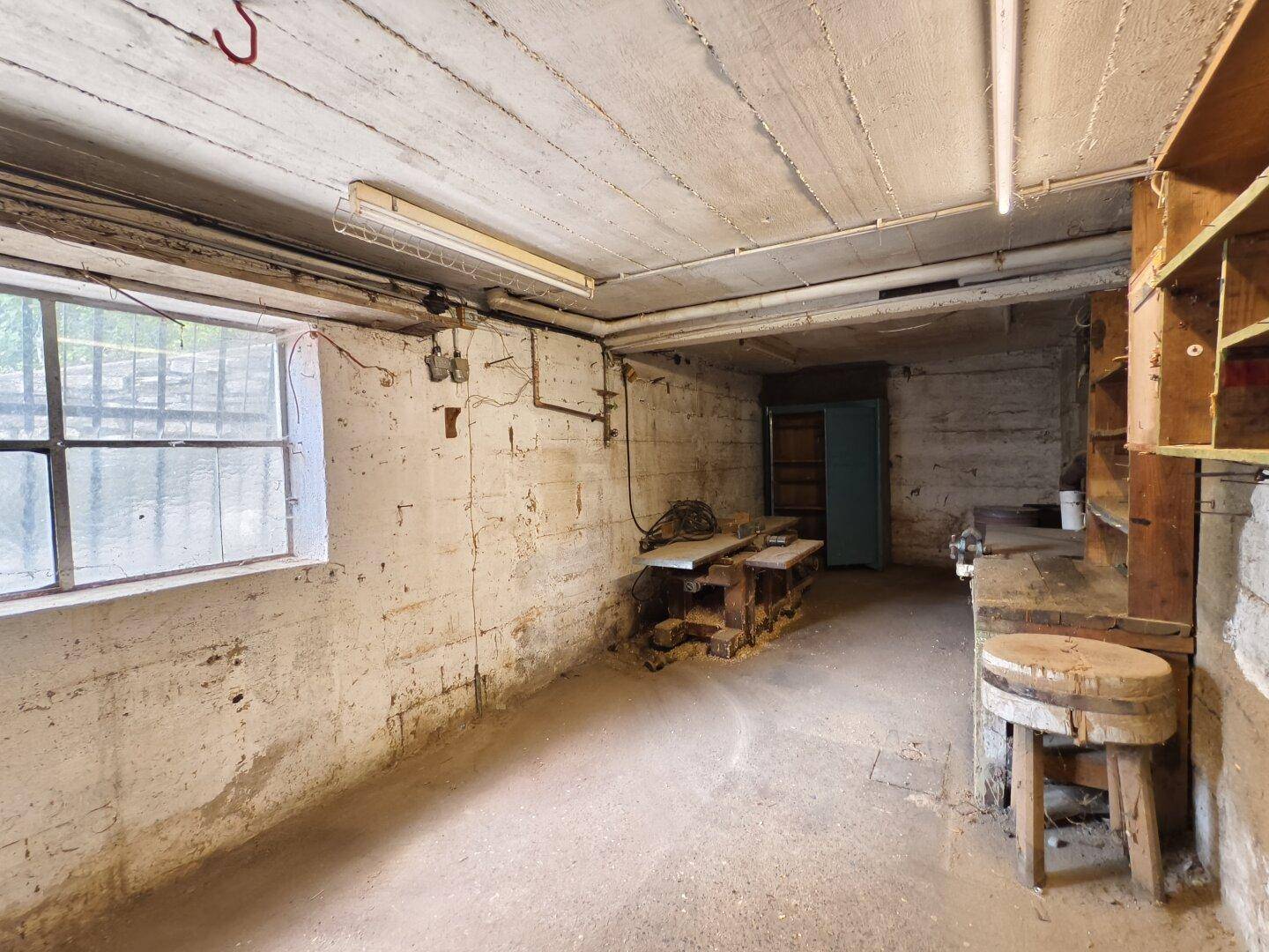 Kellerraum als Werkstatt mit Betonboden, Fenster und rustikaler Werkbank.