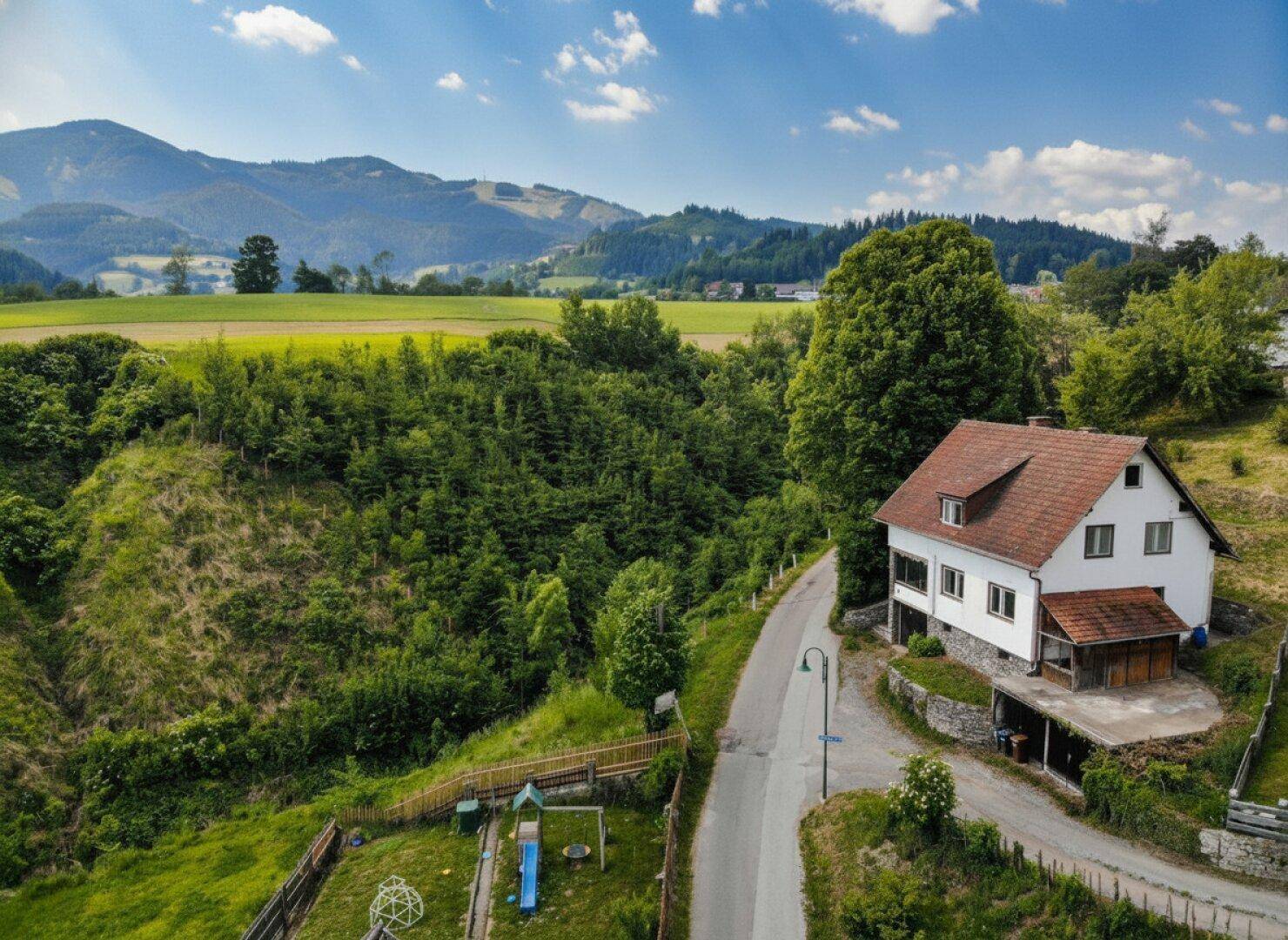 Haus in idyllischer Hügellandschaft mit angrenzendem Spielplatz und Wald.