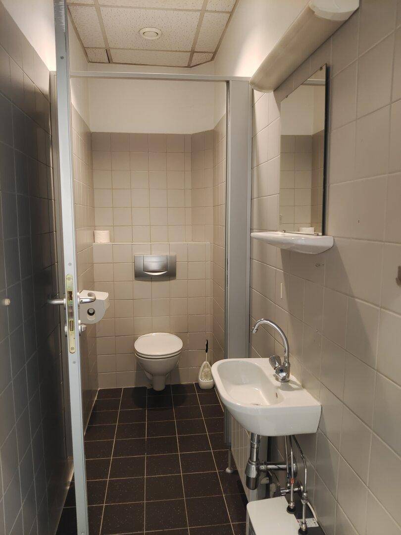 Funktionale Toilette mit Waschbecken, WC und hellen Fliesen an Wänden und Boden.