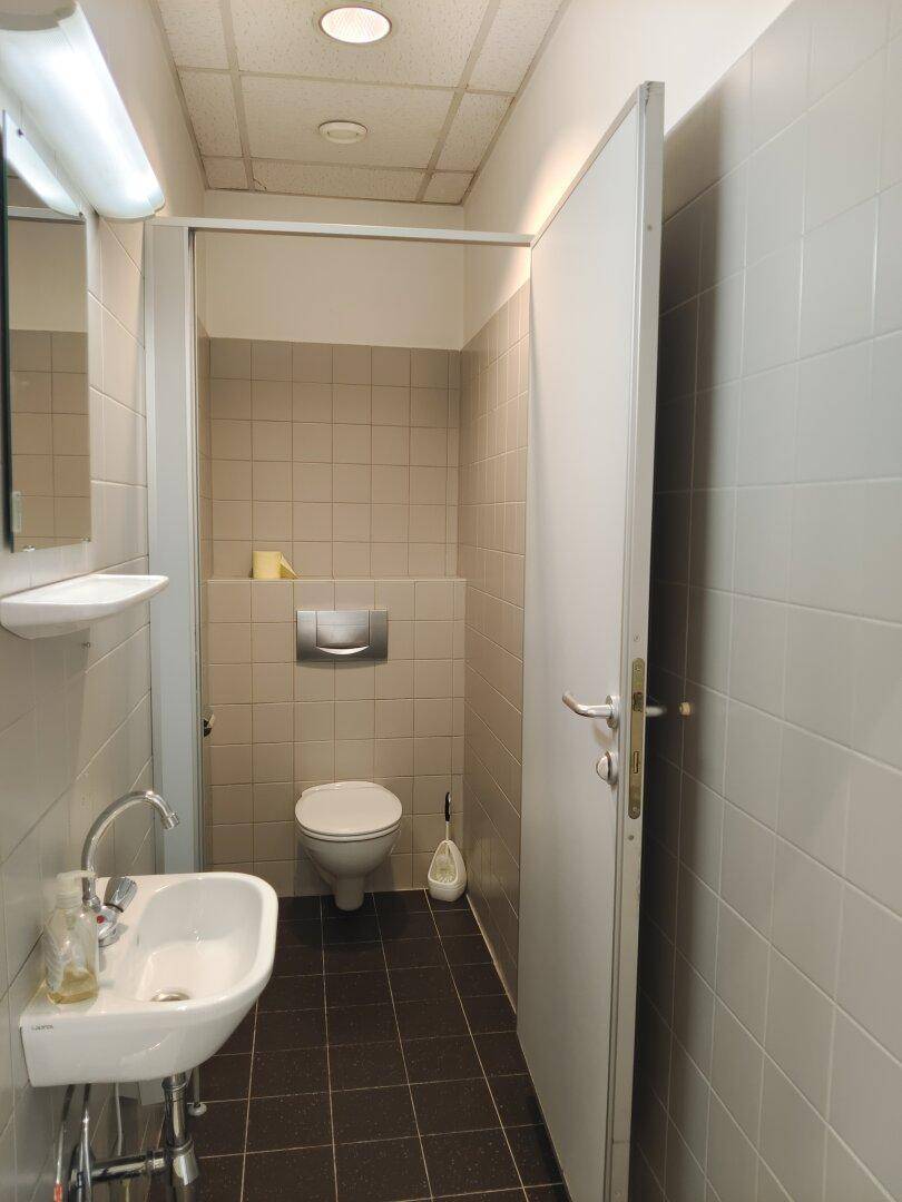 Saubere Toilette mit Waschbecken, Spiegel und hellen Wandfliesen.